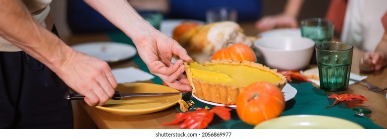 Man Cuts And Takes Piece Of American Pumpkin Pie From Table At Thanksgiving Celebration At Home With Whole Family. Long Banner.