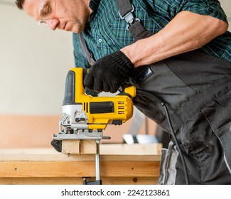 A man cuts a wooden plank with an electric jigsaw in a workshop. - Powered by Shutterstock