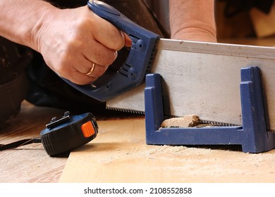 A Man Cuts A Wooden Plinth On A Plastic Stool With A Saw