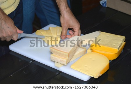Man cutting different cheese types with knife on white cuttingboard.