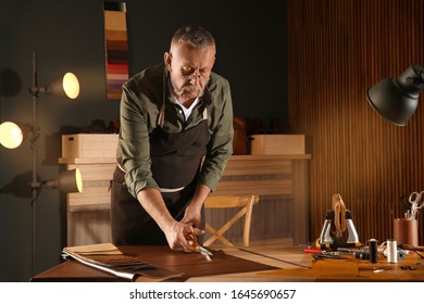 Man Cutting Leather With Scissors In Workshop