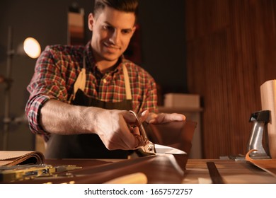 Man Cutting Leather With Scissors In Workshop