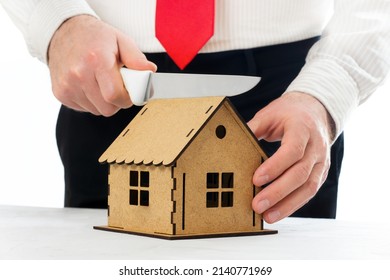 Man Cutting A Miniature House Model With A Knife. Assets Division In A Divorce.