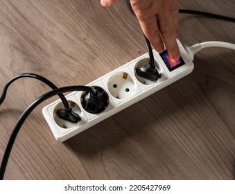 A man cutting off the electrical current by turning off the button on a white electrical socket to reduce energy consumption
