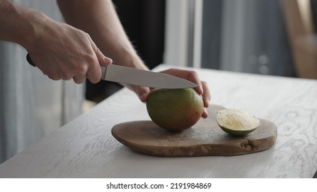 Man Cutting Ripe Mango On Olive Board On White Oak Table