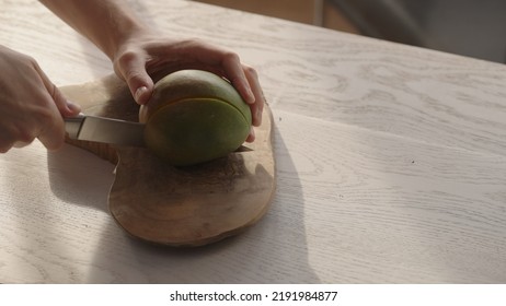 Man Cutting Ripe Mango On Olive Board On White Oak Table