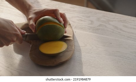 Man Cutting Ripe Mango On Olive Board On White Oak Table