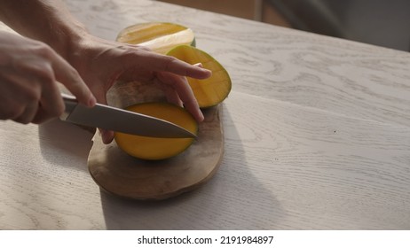 Man Cutting Ripe Mango On Olive Board On White Oak Table