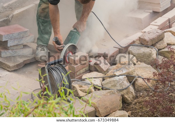 Man cutting stone slabs, concrete slab with an\
electric grinder