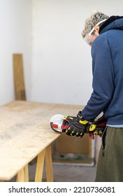 Man Cutting Wood With Electric Saw Wearing Protective Gloves And Glasses At Home. Vertical Photo