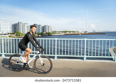 A man cycles along a waterfront path on a bright day, with a backdrop of modern buildings and a clear sky.

 - Powered by Shutterstock