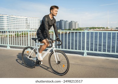 A man cycling on a bridge, with modern buildings and a serene waterfront in the background.

 - Powered by Shutterstock