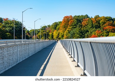 A Man Cycling On A Bridge Over Credit River On A Sunny Autumn Day With Colorful Foliage In The Background