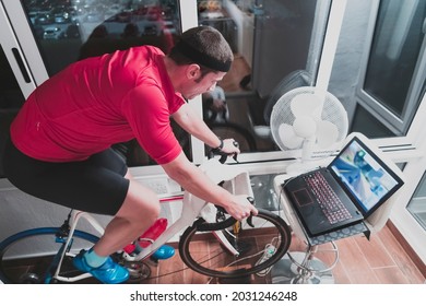 Man Cycling On The Machine Trainer He Is Exercising In The Home At Night Playing Online Bike Racing Game