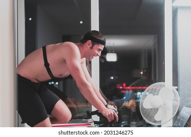 Man Cycling On The Machine Trainer He Is Exercising In The Home At Night Playing Online Bike Racing Game