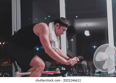 Man Cycling On The Machine Trainer He Is Exercising In The Home At Night Playing Online Bike Racing Game