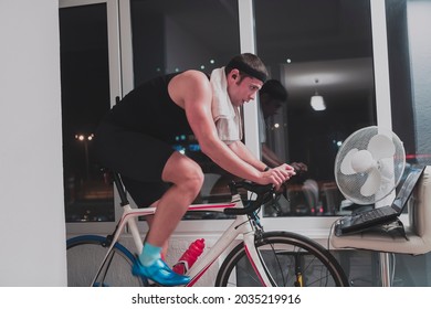 Man Cycling On The Machine Trainer He Is Exercising In The Home At Night Playing Online Bike Racing Game