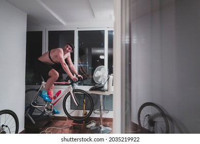 Man Cycling On The Machine Trainer He Is Exercising In The Home At Night Playing Online Bike Racing Game