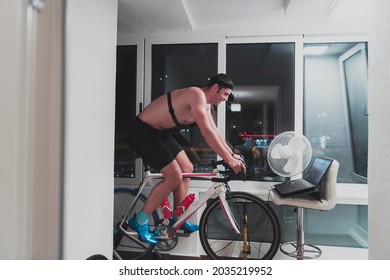 Man Cycling On The Machine Trainer He Is Exercising In The Home At Night Playing Online Bike Racing Game