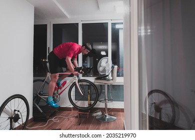 Man Cycling On The Machine Trainer He Is Exercising In The Home At Night Playing Online Bike Racing Game