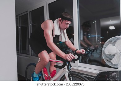 Man Cycling On The Machine Trainer He Is Exercising In The Home At Night Playing Online Bike Racing Game