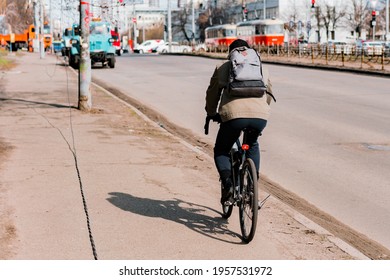 Man Cycling Through The City's Pavement In A Jacket With Grey Back Pack. Cold Weather. Sidewalk. Urban. Job. Commuting. Transport. Transportation