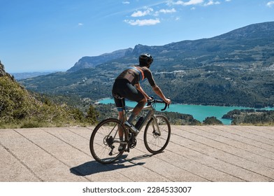 Man cyclist in helmet and cycling kit riding through mountainous roads. Cyclist on gravel bike with scenic views of turquoise lake in Spain.Gravel riding through the mountains.Guadalest Reservoir. - Powered by Shutterstock