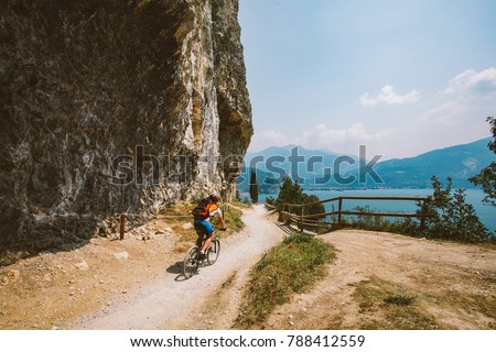 man cyclist on a mountain bike riding on a gravel bike route at a height near the Lago di Garda in summer in Italy.