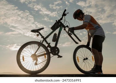 Man cyclist repairing a bike against the background of sky  - Powered by Shutterstock