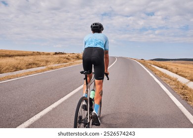 Man cyclist riding on an empty road, enjoying a scenic cycling route. The blue sky and golden fields create a picturesque backdrop for the active lifestyle. Cycling hobby - Powered by Shutterstock