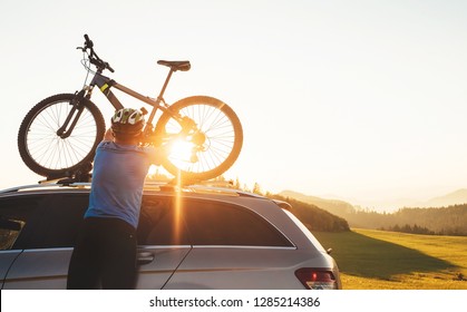 Man Cyclist Veared In Cycling Clothes And Protective Helmet Instals His Mountain Bike On The Car Roof