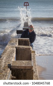 man daring to be splashed by wave on groyne in bay