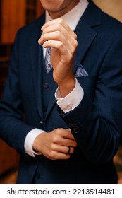 A Man In A Dark Blue Suit And Straightens His Shirt Sleeve