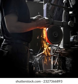 Man in a dark forge grinding a knife with a belt grinder with sparks flying downwards - Powered by Shutterstock