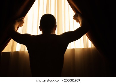 Man In Dark Room Opens Curtains On Window To The Morning Light