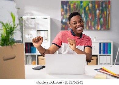 Man With Dark Skin In Tshirt Is Satisfied With Sold Service Products, Happy With The Monthly Profits, Sitting In Front Of Computer Victory Dance, Hands Clenched Into Fists Looking Into Camera, Smiling