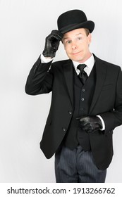 Man In Dark Suit And Leather Gloves Doffing Bowler Hat On White Background. Concept Of Classic And Eccentric British Gentleman Stereotype. Retro Style And Vintage Fashion.