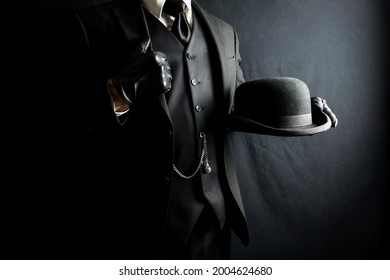 Man In Dark Suit And Leather Gloves Holding Bowler Hat On Black Background. Concept Of Classic And Eccentric British Gentleman Stereotype. Retro Style And Vintage Fashion.