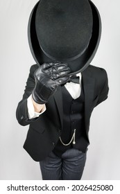 Man In Dark Suit And Leather Gloves Politely Doffing Bowler Hat On White Background. Concept Of Classic And Eccentric British Gentleman Stereotype. Retro Style And Vintage Fashion.