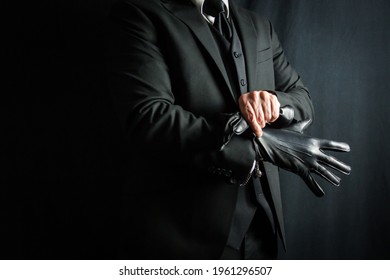 Man in Dark Suit Putting on Leather Gloves on Black Background. Concept of Classic and Eccentric British Gentleman Stereotype. Retro Style and Vintage Fashion.