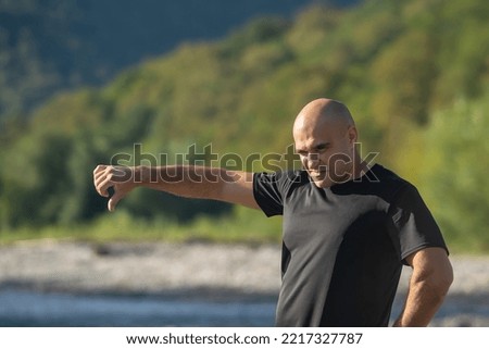 a man in a dark T-shirt stands in nature against the backdrop of mountains and a river, twisted his face and shows a sign with his hand, thumb down, everything is bad Stock foto © 