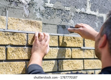 Man decorates the facade of the fence with decorative torn bricks, close up view. Work at home during quarantine, DIY
