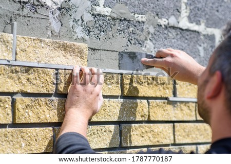 Man decorates the facade of the fence with decorative torn bricks, close up view. Work at home during quarantine, DIY