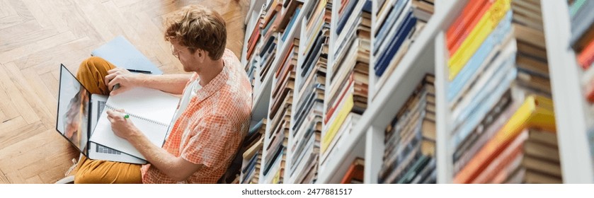 A man, deep in concentration, writes in a library.