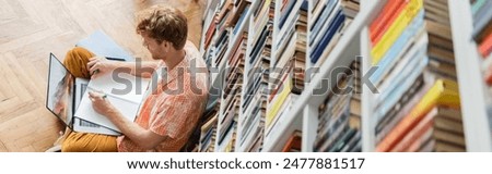 A man, deep in concentration, writes in a library.