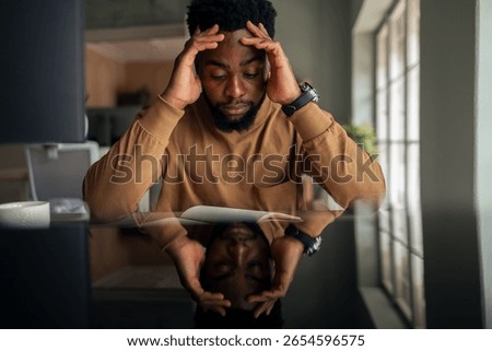 A man deep in thought, reading a document at a reflective table in a modern office setting.