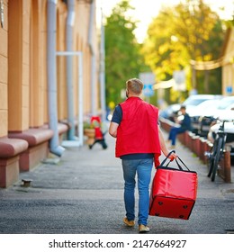 Man deliver food, walk with red backpack delivering online food orders to costumers. Сourier deliver food order walking along narrow street of old city. Man carrying red bag with food orders. - Shutterstock ID 2147664927