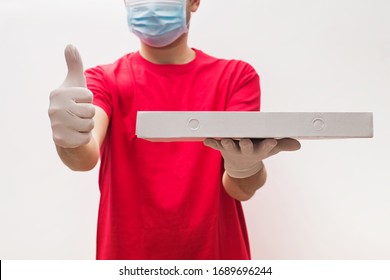 Man from delivery service in red t-shirt, wearing protective mask and gloves holding pizza box in one hand and showing thumb up. Contactless, safe pizza delivery during virus outbreak.