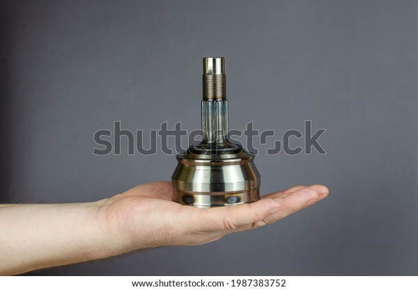 A man demonstrates a Drive shaft joint against a\
gray background. New Constant velocity joints.  Spare parts,\
consumables. Side view.