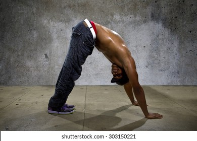 Man Demonstrating Core Balance Exercises Or Yoga On Urban Background. He Is Dressed In Hip Hop Style Clothing But Shirtless To Show Off Muscles.